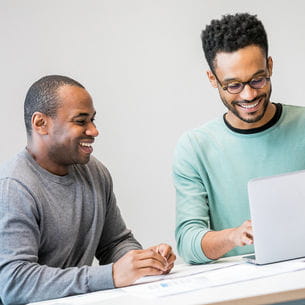 Two people sat at a table using a laptop.