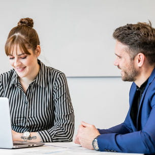 Two people working on a laptop in a meeting room.