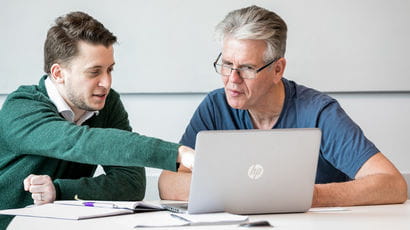 Two people working on a laptop in a meeting room.