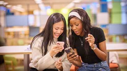 A couple of female students leaning heads together looking at their mobiles.