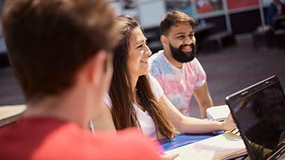 Three undergraduate students outside, studying in front of a laptop.