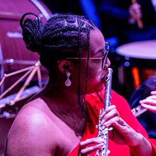 Woman in elegant outfit playing flute in a darkened concert hall. 