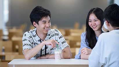 A group of international students, laughing with each other whilst sat around a table.