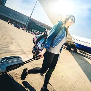 Woman pulling a suitcase across the tarmac next to a plane