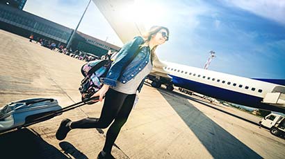 Woman smiling pulling a suitcase next to a plane