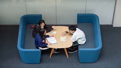 Three students sat on sofas working together across a table