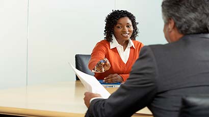 A man and a woman sat across the table from each other discussing a document that is being pointed at