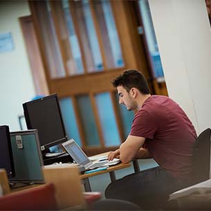 Male student working at a laptop, surrounded by PCs