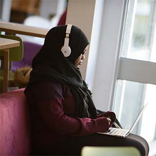 Female student wearing headphones working on a laptop