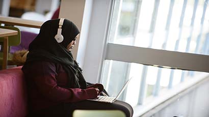 Female student wearing headphones working on a laptop