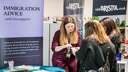 Two female students chatting with an immigration adviser at a conference