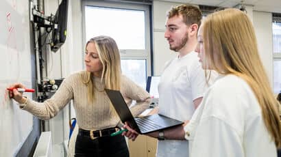 Three students working together on a project and writing down ideas on a whiteboard.