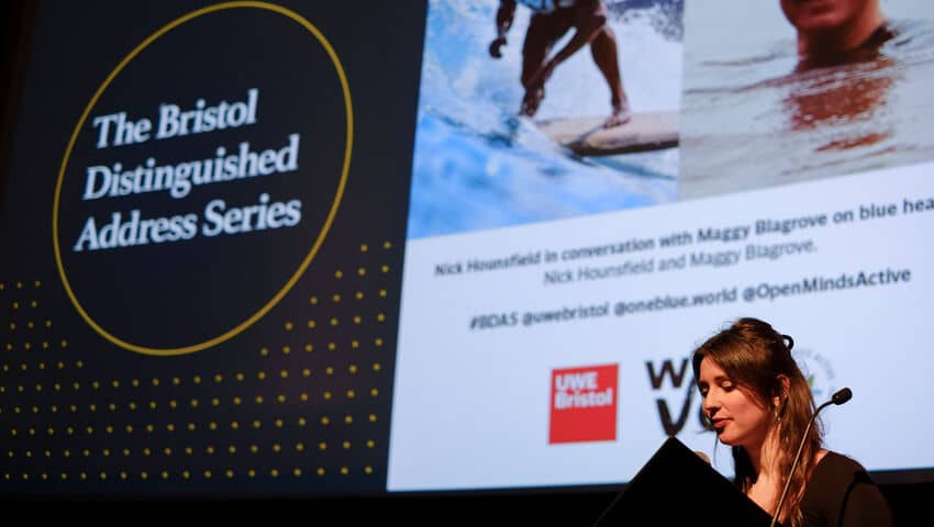 A white woman at a lectern with a screen behind her. 