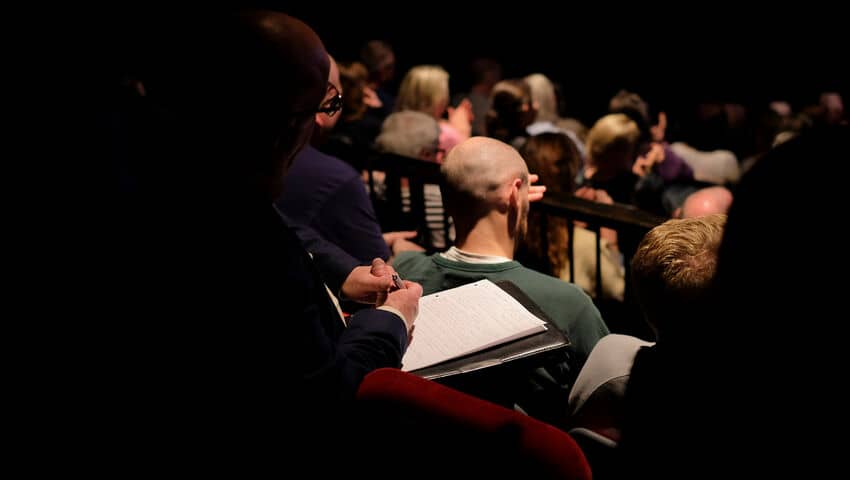 An audience from the back in red velvet chairs.