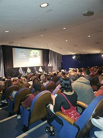 View over the busy audience towards the panel members on stage at The Watershed.