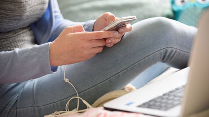 Student using a mobile next to a laptop