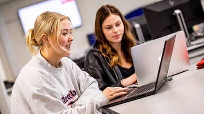 Two students working on their laptops at a table.