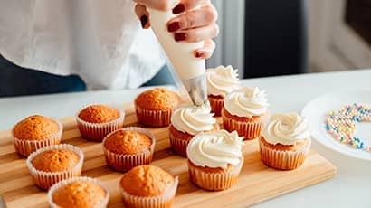 A person decorating small cakes with icing