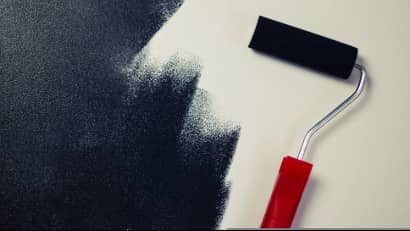 A white wall being painted black with a large roller.