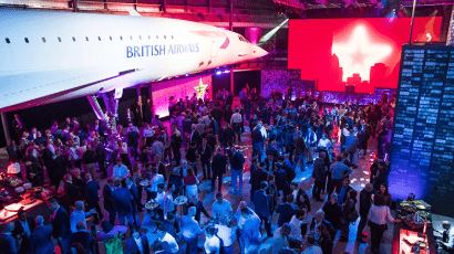 A crowd of people mingling under Concorde.