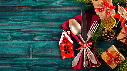 A selection of Christmas table items including knife and fork tied with red ribbon and miniature gift wrapped boxes.