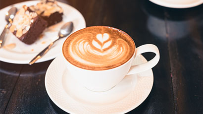 A fresh cappuccino in a cup and saucer with brownies in the background.