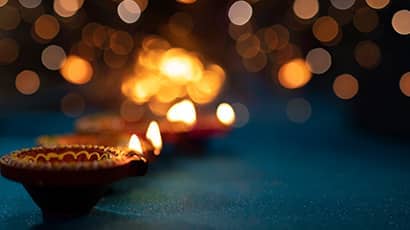 Three Diwali candles on a dark blue table with lights soft in the background.