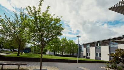 Exterior of S block with a row of trees against a cloudy blue sky.