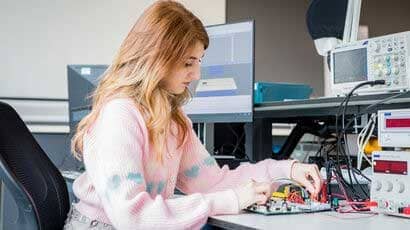 Female student working on a circuit board next to a pc.