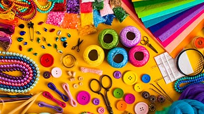 A selection of brightly coloured crafting materials including buttons, scissors, ribbons, paper and beads.