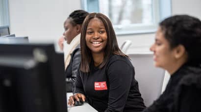 Three black female students smiling and working on PCs.