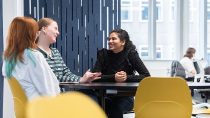 Three students sat around in a study space having a discussion