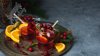 Two Christmas mocktail glasses on a plate full of orange slices and berries.