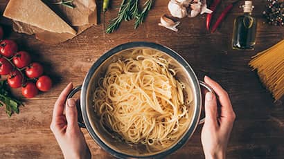 A pot of pasta with lots of herbs and spices around it.