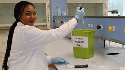 A student working in a laboratory and discarding waste into the plastic recycling only bin