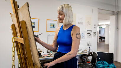 Student standing in the Drawing Centre painting on an easel.