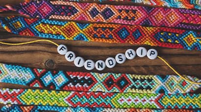 Colourful friendship bracelets laid out on the table, one with beads spelling out the word 'friendship'.