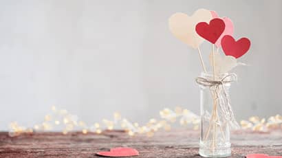 A small glass with heart sticks on a wooden table with heart shape papers. 