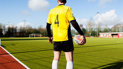 A young man in a football uniform standing on the football field while holding a soccer ball.