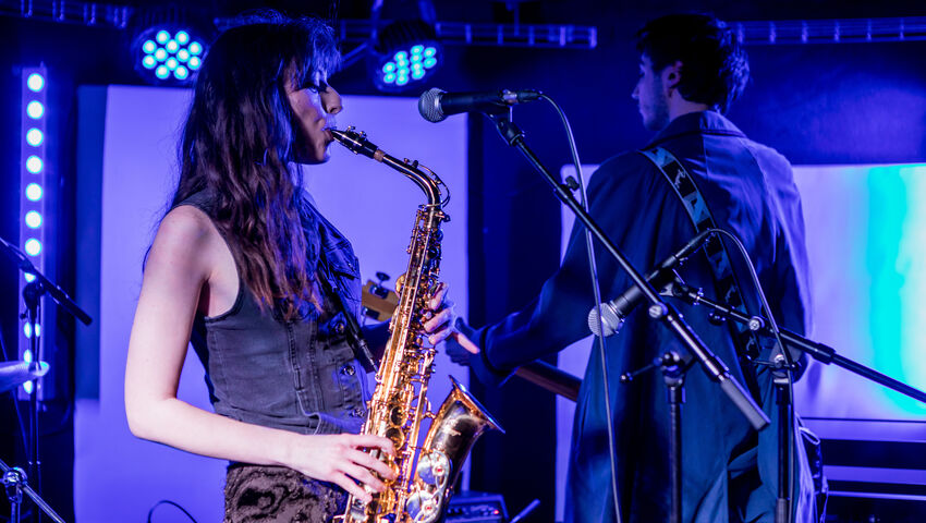 Performers on stage at The Louisiana playing a saxophone and guitar.