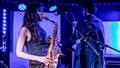 Performers on stage at The Louisiana playing a saxophone and guitar.