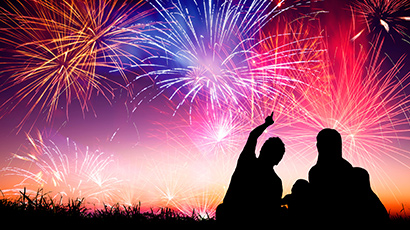 Two people silhouetted against a sky of colourful fireworks.