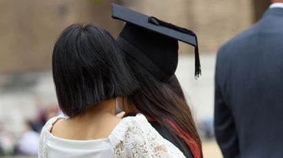 Graduand at her Awards Ceremony wearing robes while standing next to family.