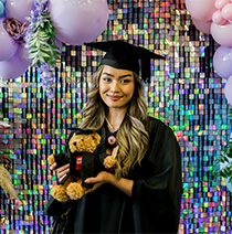 Graduate posing with teddy bear dressed in graduation robes