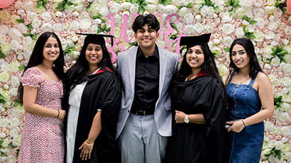 Two graduates and three guests posing together in front of UWE Bristol's flower display