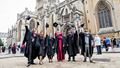 A group of graduates raising their caps outside Bristol Cathedral