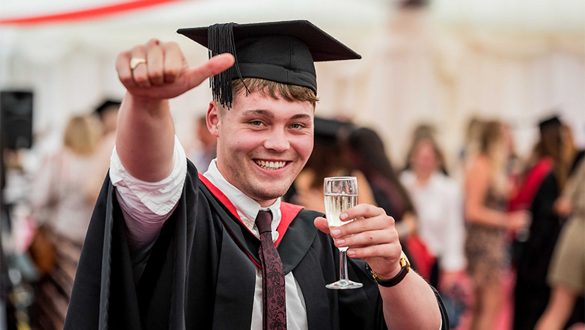 Graduate celebrating after graduation with a glass of champagne in the marquee