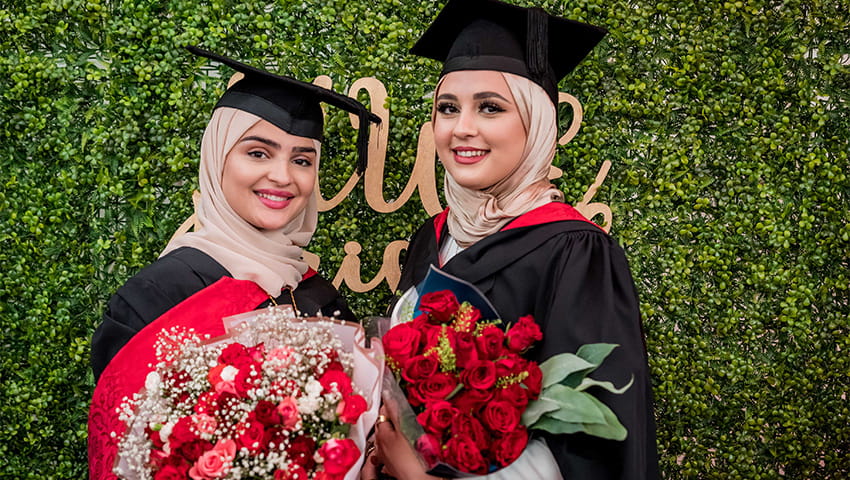 Two graduates smiling and holding a bouquet of flowers