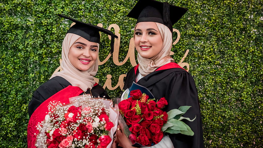 Two graduates smiling and holding a bouquet of flowers