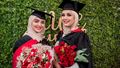Two graduates smiling and holding a bouquet of flowers